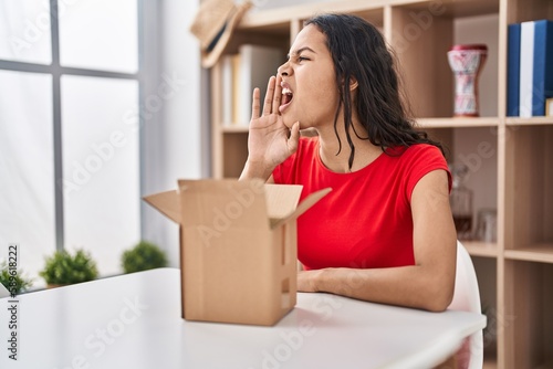 Young brazilian woman looking inside cardboard box clueless and confused with open arms, no idea and doubtful face.