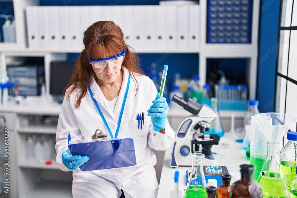 Middle age woman scientist reading report holding test tube at laboratory Middle age woman scientist reading report holding test tube at laboratory