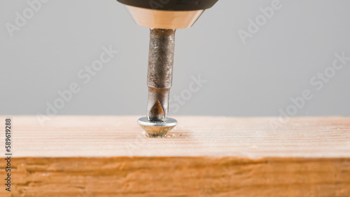 Fotografie Screwdriver tightening screw in wood close up