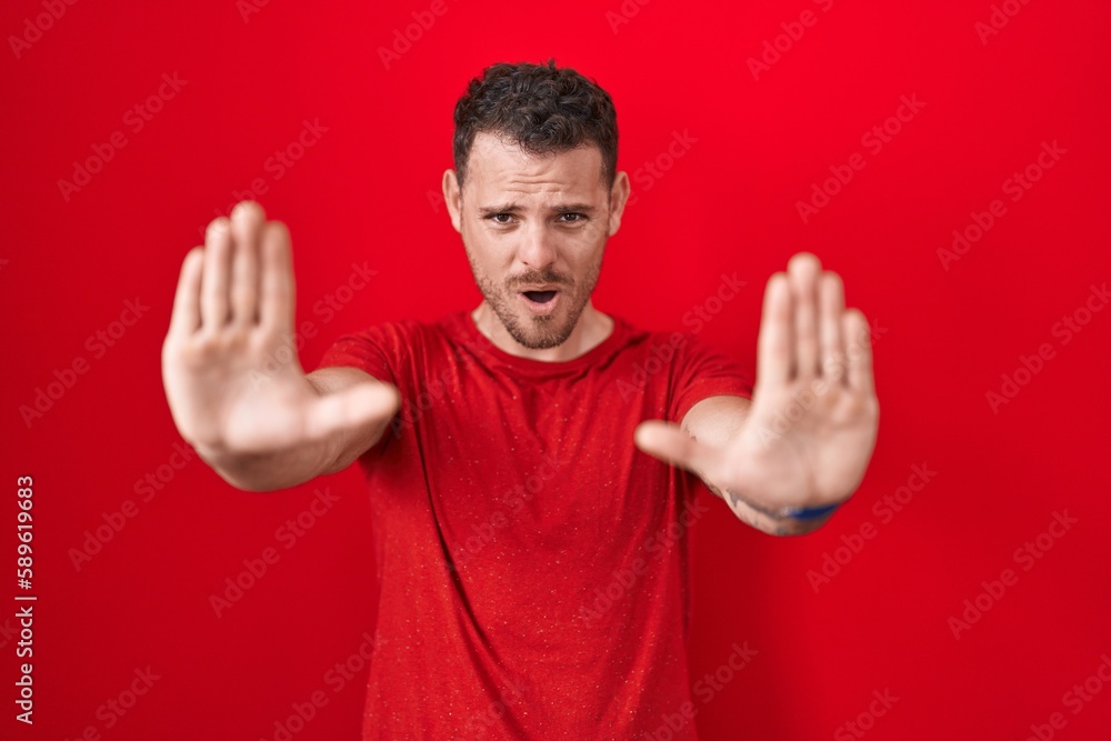 Young hispanic man standing over red background doing stop gesture with hands palms, angry and frustration expression Young hispanic man standing over red background doing stop gesture with hands palms, angry and frustration expression
