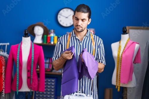 Young hispanic man tailor holding cloths at sewing studio photo