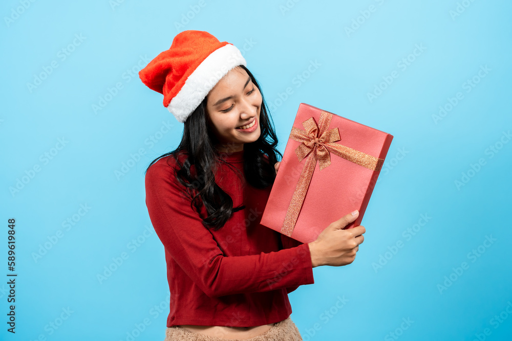 portrait, Long-haired asian girl red long-sleeved top wearing christmas hats, was pulling gift box another person hand family fun handing out presents, Isolated indoor studio on blue background. portrait, Long-haired asian girl red long-sleeved top wearing christmas hats, was pulling gift box another person hand family fun handing out presents, Isolated indoor studio on blue background.
