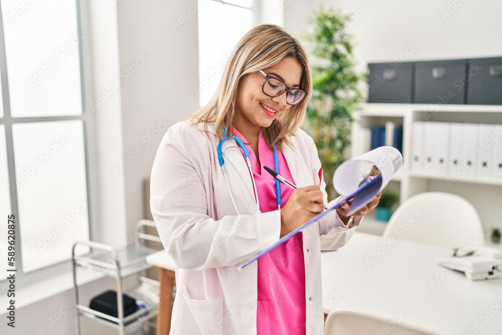 Young hispanic woman wearing doctor uniform writing on clipboard al clinic Young hispanic woman wearing doctor uniform writing on clipboard al clinic