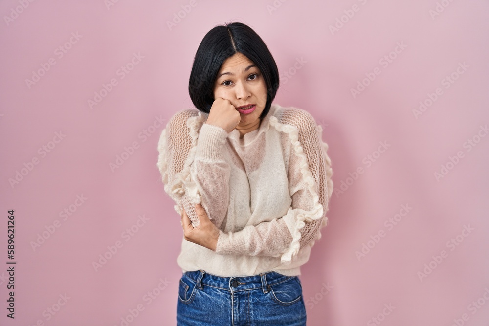 Young asian woman standing over pink background looking stressed and nervous with hands on mouth biting nails. anxiety problem. Young asian woman standing over pink background looking stressed and nervous with hands on mouth biting nails. anxiety problem.