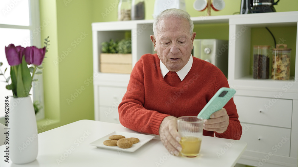 senior eating cookies and drinking juice using smartphone at home senior eating cookies and drinking juice using smartphone at home