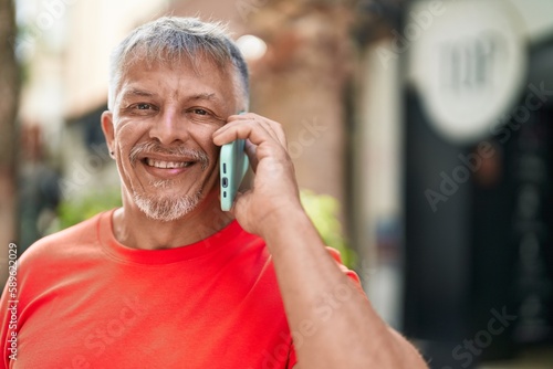 Middle age grey-haired man smiling confident talking on the smartphone at street