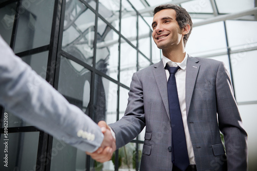 Businessmen shake hands, standing near a large office window