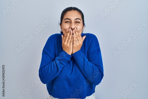 фотографія Young hispanic woman standing over isolated background laughing and embarrassed