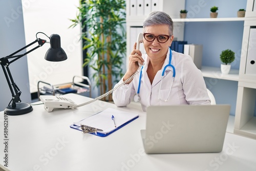 Middle age woman wearing doctor uniform talking on the telephone at clinic