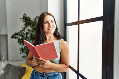 Young beautiful hispanic woman smiling confident reading book at home