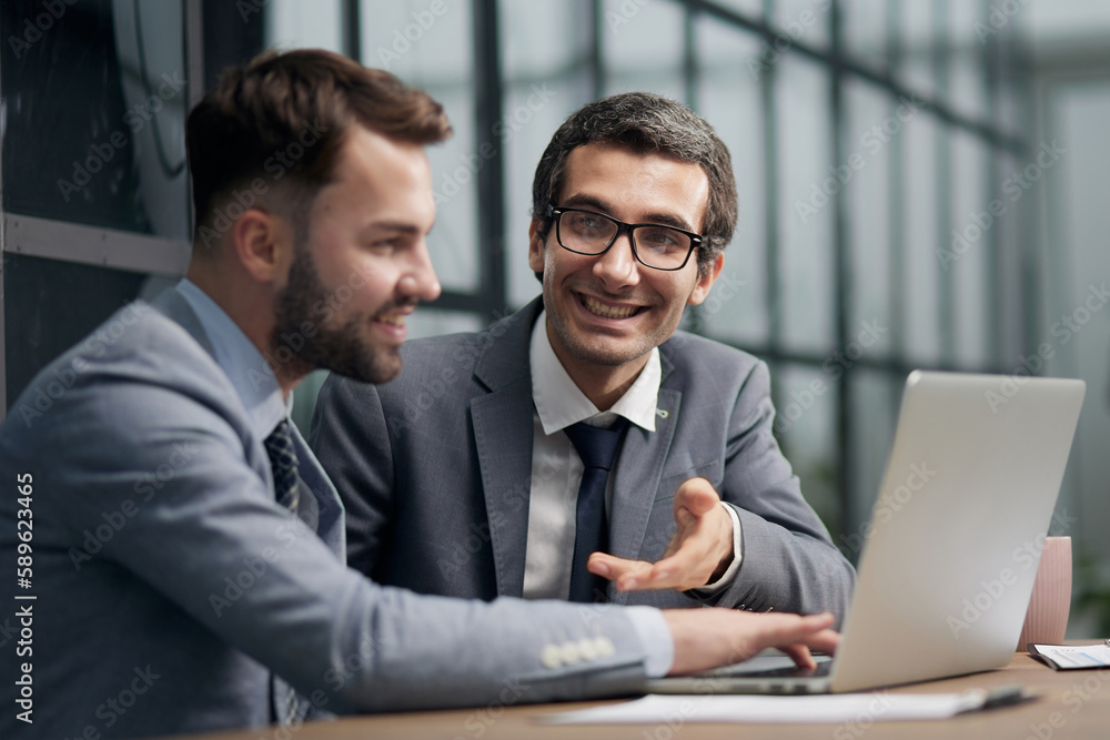 Obraz premium Two young businessmen sitting at workplace and working together in office