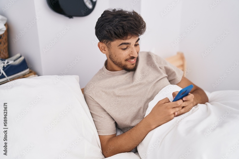 Obraz premium Young arab man using smartphone sitting on bed at bedroom