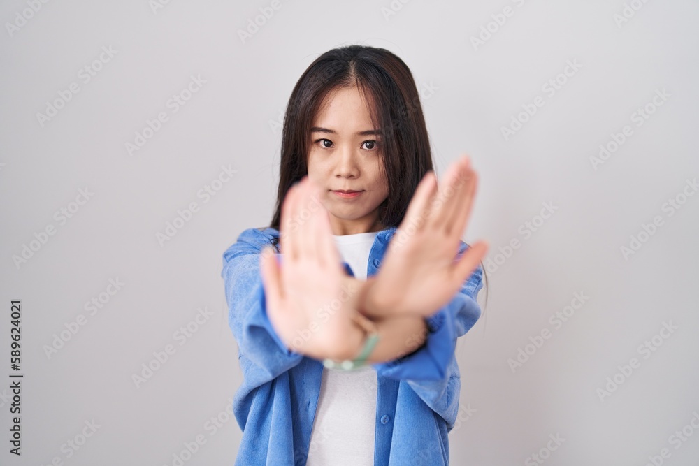 Young chinese woman standing over white background rejection expression crossing arms and palms doing negative sign, angry face