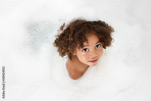 Top view of little girl with afro hair in bubble bath looking up