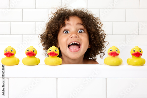 Funny young girl with afro hair playing in bathtub with rubber ducks making funny face photo