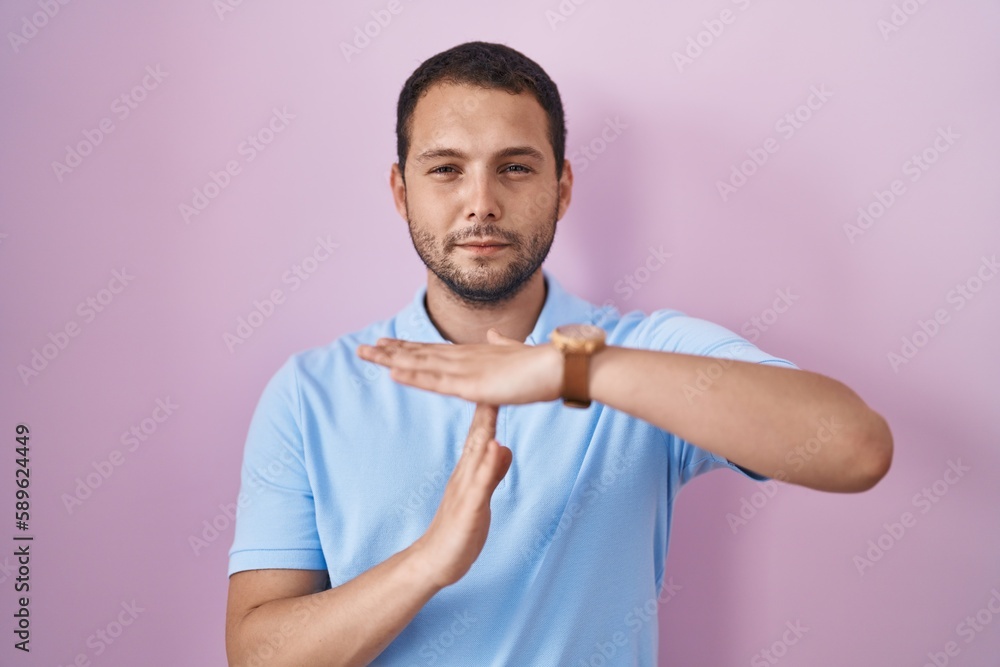 Hispanic man standing over pink background doing time out gesture with hands, frustrated and serious face Hispanic man standing over pink background doing time out gesture with hands, frustrated and serious face