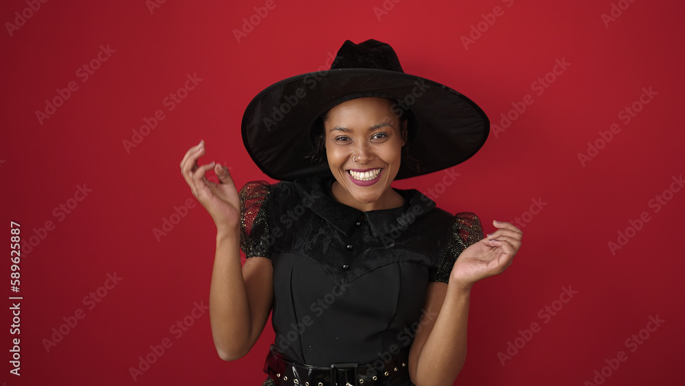 African american woman wearing witch costume having halloween party over isolated red background African american woman wearing witch costume having halloween party over isolated red background