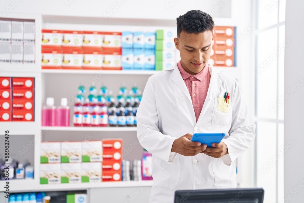 Young latin man pharmacist smiling confident using touchpad at pharmacy