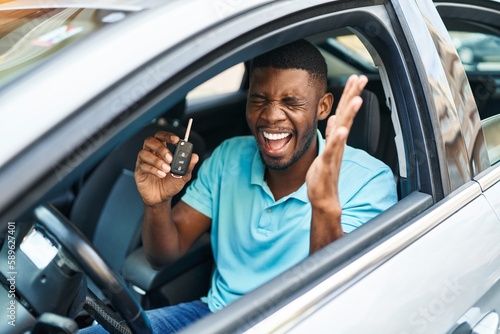 Young african american man holding key of new car with cheerful expression at street