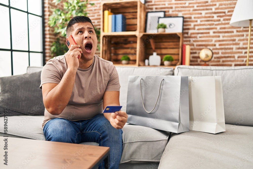 Hispanic young man doing payment with credit card on the phone angry and mad screaming frustrated and furious, shouting with anger looking up. Hispanic young man doing payment with credit card on the phone angry and mad screaming frustrated and furious, shouting with anger looking up.