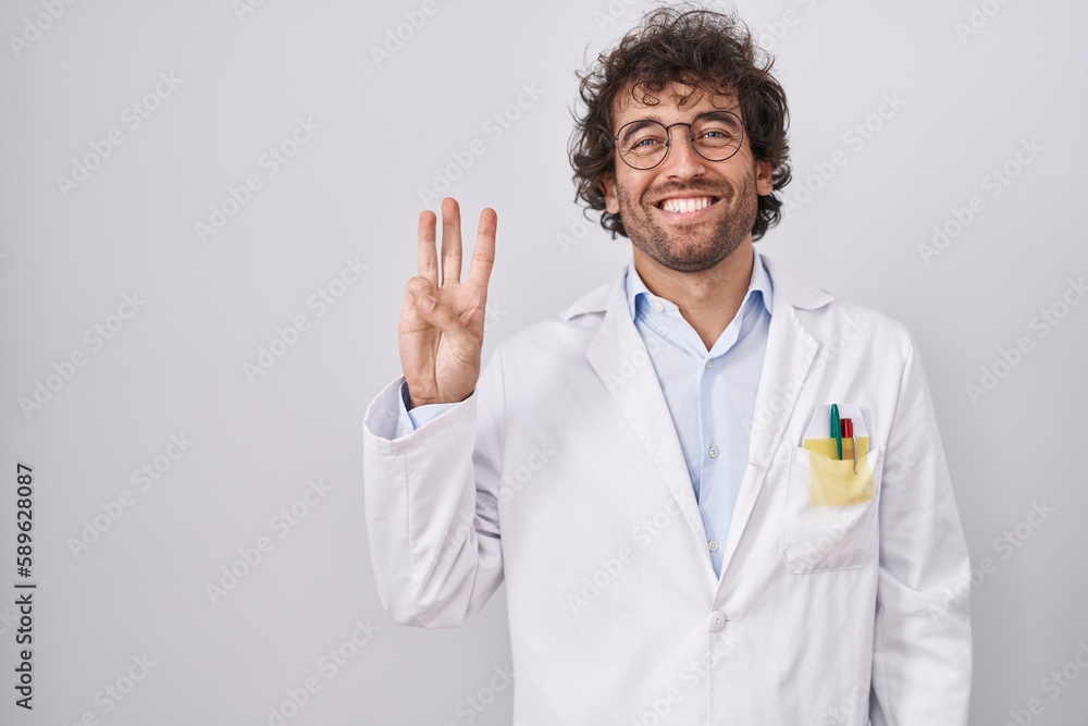 Hispanic young man wearing doctor uniform showing and pointing up with fingers number three while smiling confident and happy. Hispanic young man wearing doctor uniform showing and pointing up with fingers number three while smiling confident and happy.