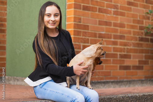 Young latin woman smiling and sitting with hers two pinscher puppies looking absently in the opposite direction photo