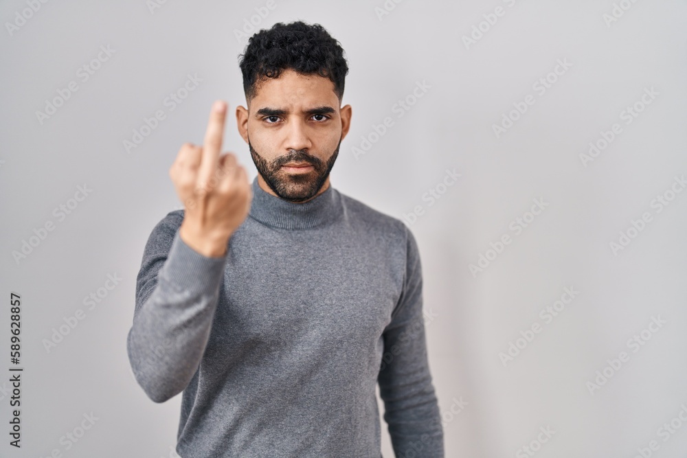 Hispanic man with beard standing over white background showing middle finger, impolite and rude fuck off expression Hispanic man with beard standing over white background showing middle finger, impolite and rude fuck off expression