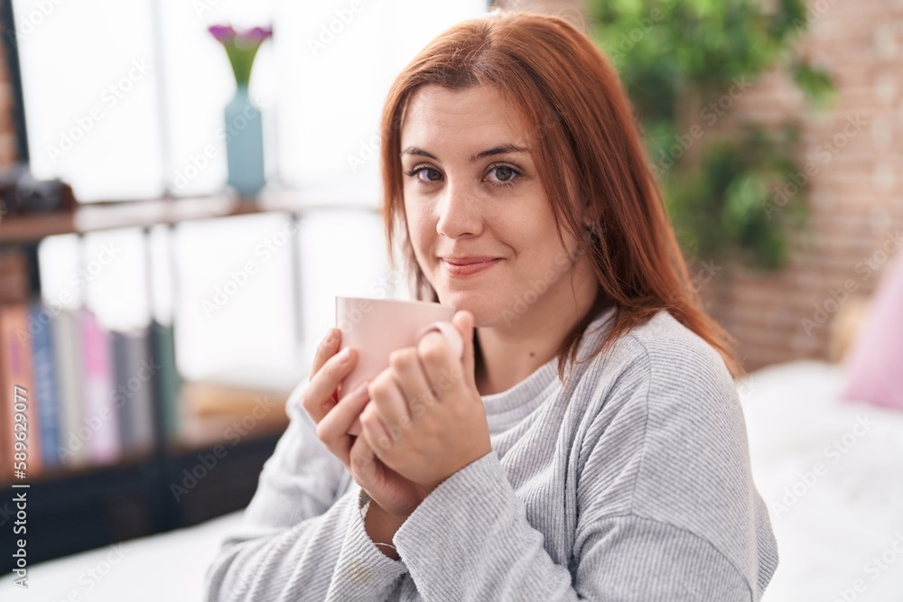 Young beautiful plus size woman drinking cup of coffee sitting on bed at bedroom Young beautiful plus size woman drinking cup of coffee sitting on bed at bedroom