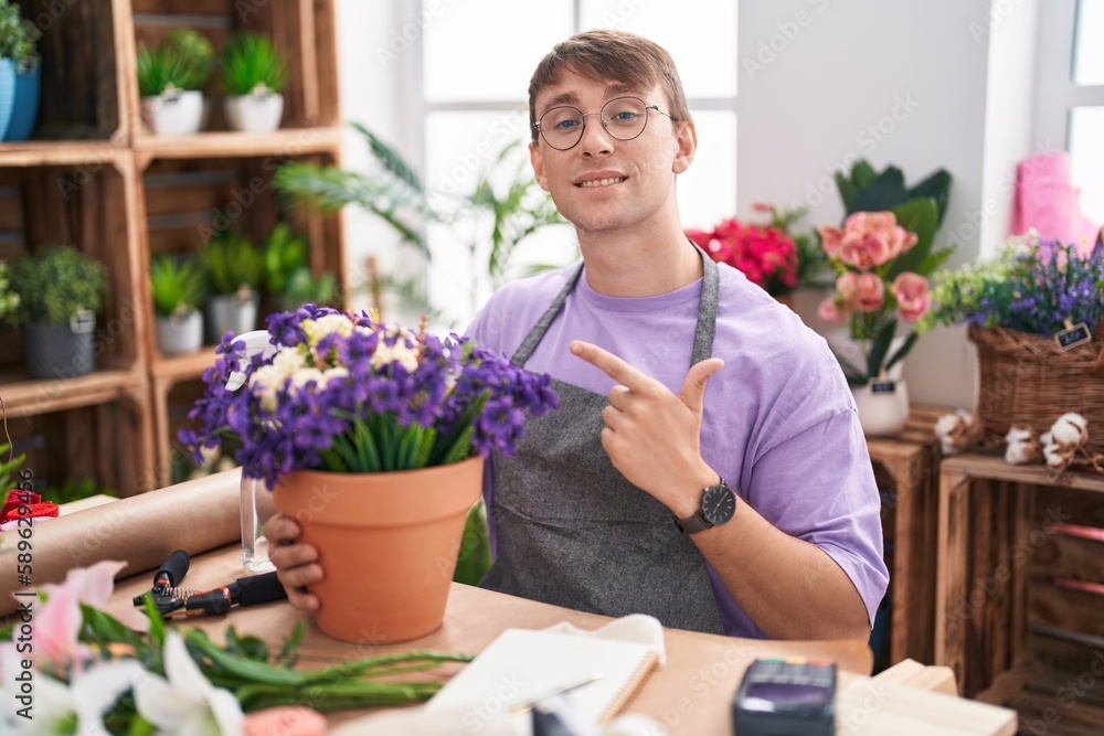 Caucasian blond man working at florist shop cheerful with a smile on face pointing with hand and finger up to the side with happy and natural expression