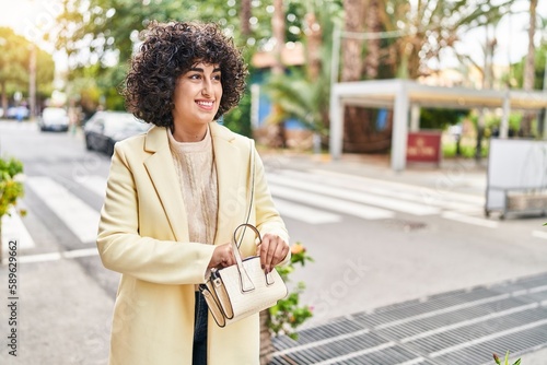 Young middle east woman excutive smiling confident holding handbag at street