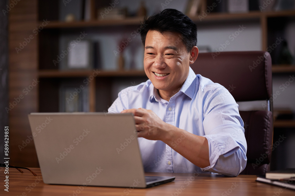 Asian man holding online webinar using laptop webcam, sitting in a home office. Man having online meeting and communicating remotely, looking at computer screen Asian man holding online webinar using laptop webcam, sitting in a home office. Man having online meeting and communicating remotely, looking at computer screen