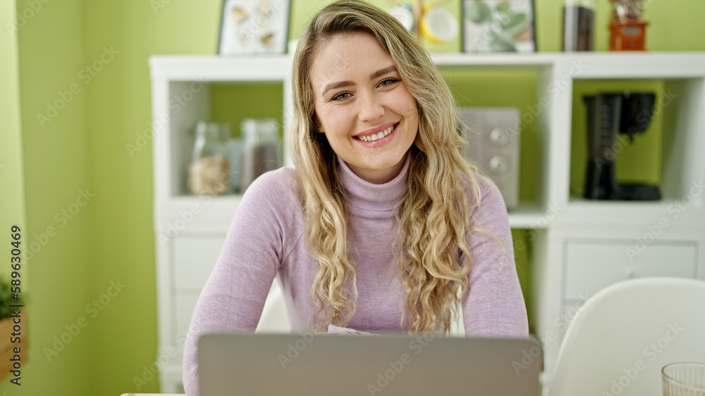 Young blonde woman using laptop sitting on table at dinning room Young blonde woman using laptop sitting on table at dinning room