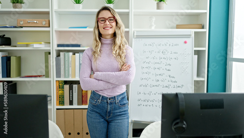 Young blonde woman teacher smiling confident standing with arms crossed gesture at classroom