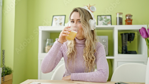 Young blonde woman drinking orange juice listening to music at dinning room