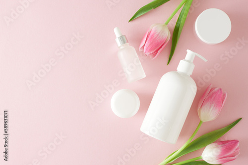 Organic beauty products concept. Top view photo of cosmetic pump bottle without label cream jars dropper bottle and pink tulips on isolated pastel pink background with copy space
