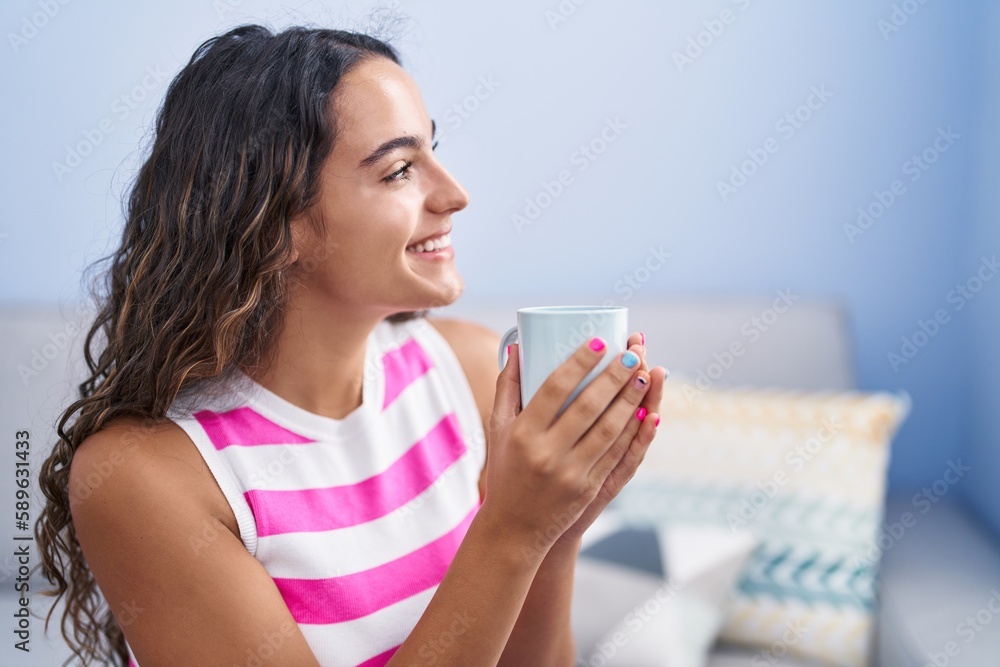 Young beautiful hispanic woman drinking coffee sitting on sofa at home Young beautiful hispanic woman drinking coffee sitting on sofa at home