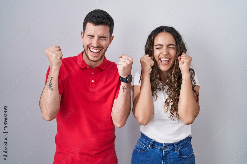 Young hispanic couple standing over isolated background excited for success with arms raised and eyes closed celebrating victory smiling. winner concept. Young hispanic couple standing over isolated background excited for success with arms raised and eyes closed celebrating victory smiling. winner concept.