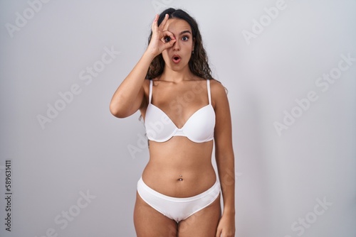 Young hispanic woman wearing white lingerie doing ok gesture shocked with surprised face, eye looking through fingers. unbelieving expression. © Krakenimages.com