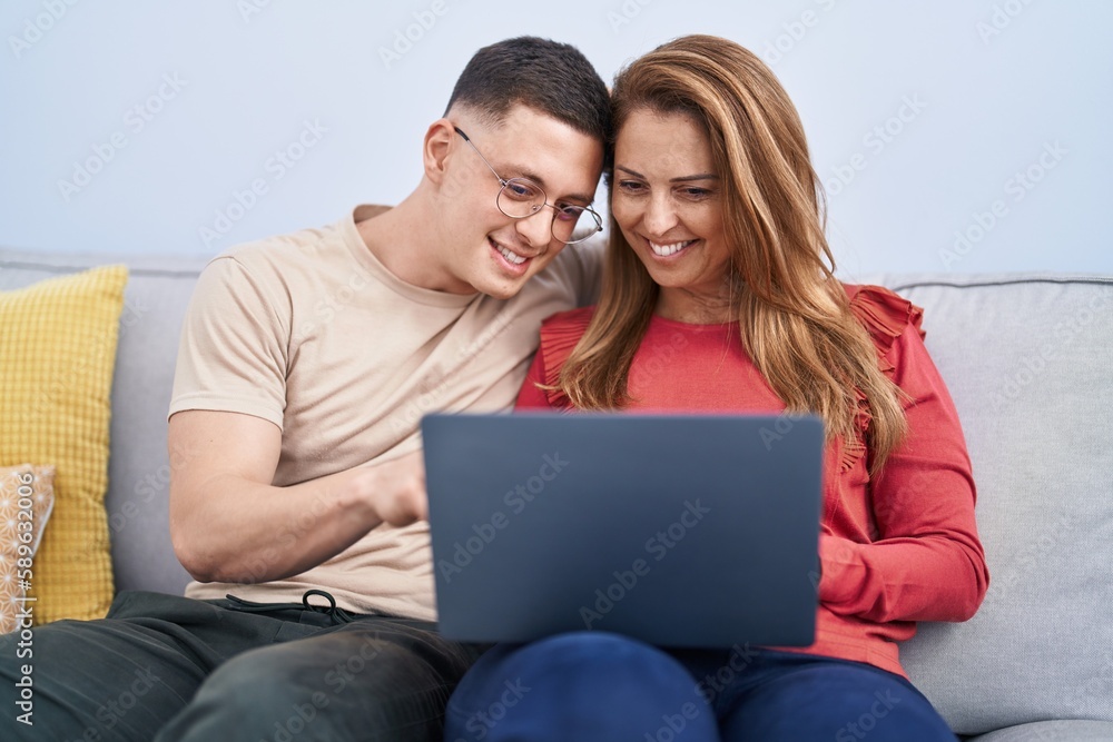 Man and woman mother and son using laptop sitting on sofa at home Man and woman mother and son using laptop sitting on sofa at home
