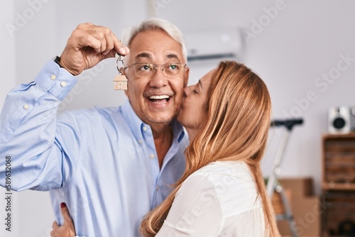 Middle age man and woman couple hugging each other holding key of new house at new home
