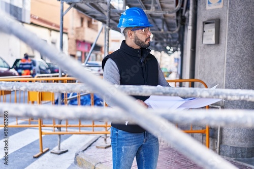 Young latin man architect holding blueprints at street
