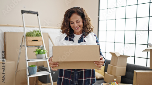 Middle age hispanic woman smiling confident holding package at new home