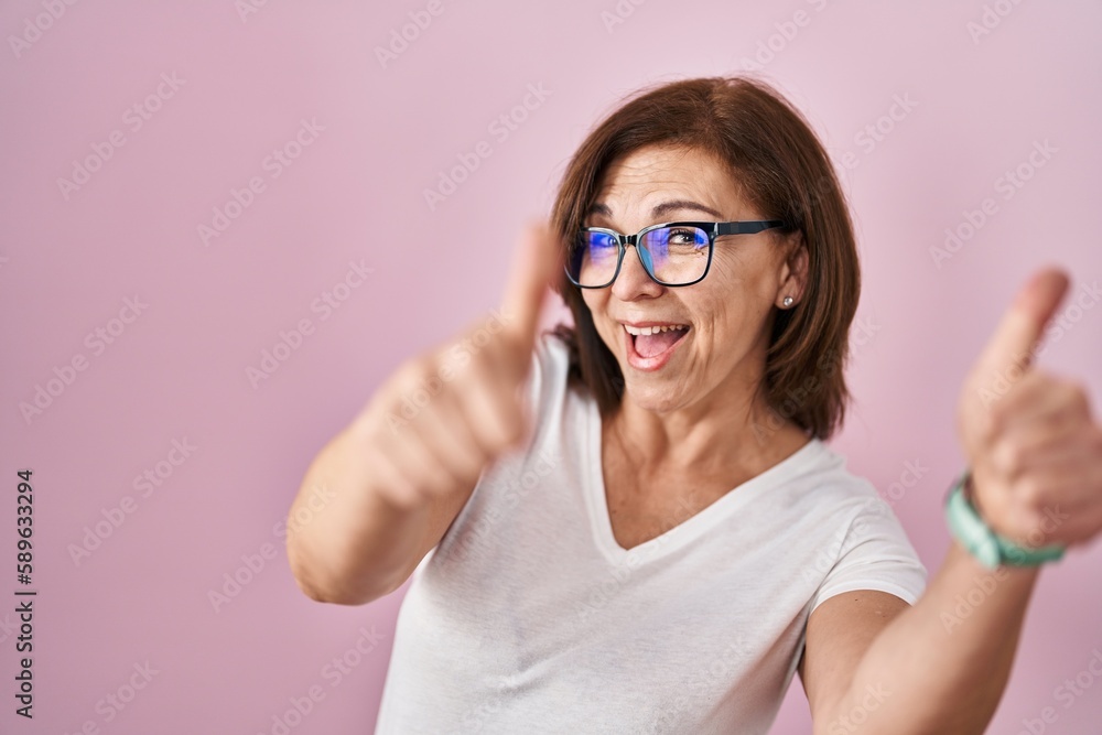 Middle age hispanic woman standing over pink background approving doing positive gesture with hand, thumbs up smiling and happy for success. winner gesture.