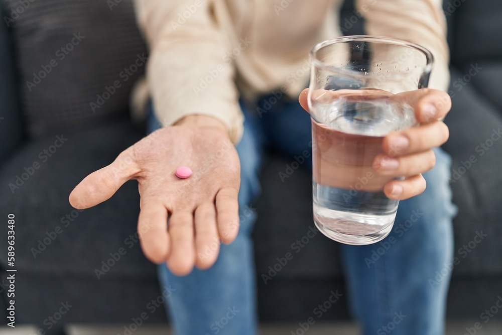 Young caucasian man holding pill and glass of water at psychology clinic