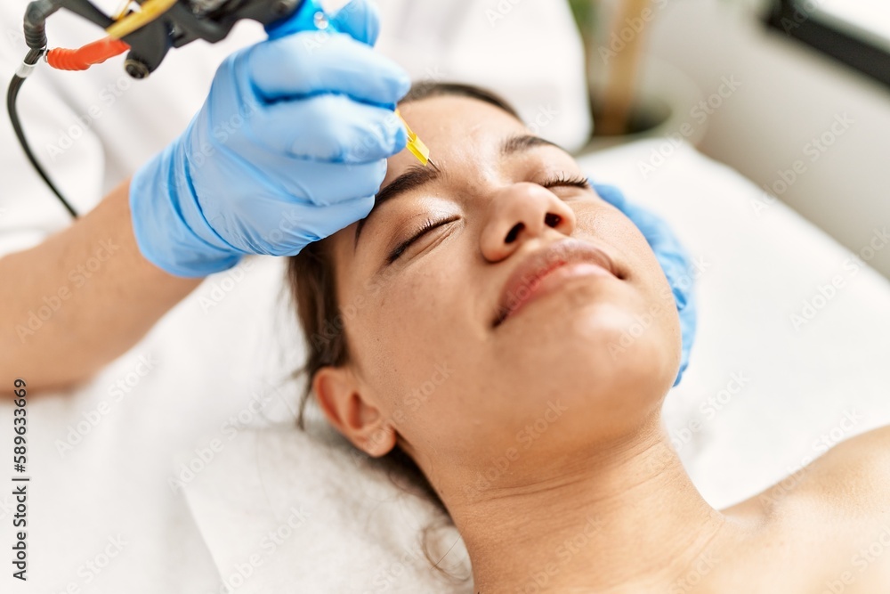 Obraz premium Young latin woman relaxed having microblading eyebrows treatment at beauty center