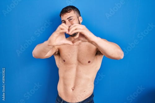 Handsome hispanic man standing shirtless smiling in love doing heart symbol shape with hands. romantic concept.