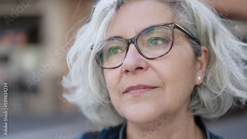 Middle age woman with grey hair standing with serious expression at street