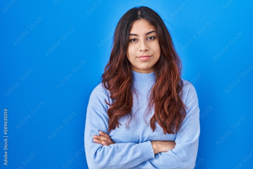 Hispanic young woman standing over blue background skeptic and nervous, disapproving expression on face with crossed arms. negative person. Hispanic young woman standing over blue background skeptic and nervous, disapproving expression on face with crossed arms. negative person.