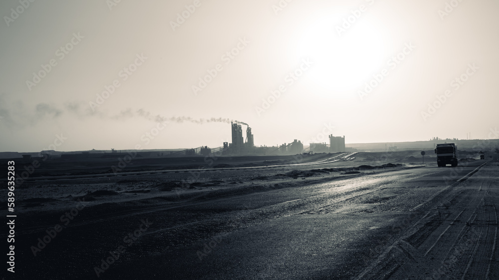 silhouette of the cement factory in the middle of the desert and the smoke rising high and stretching long away from it