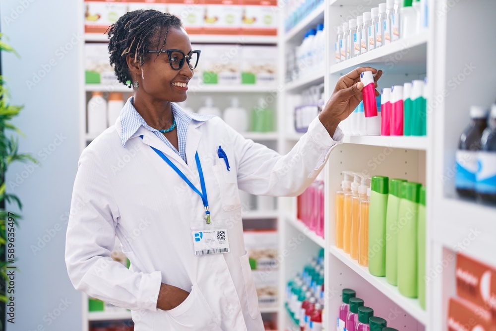 Middle age african american woman pharmacist smiling confident holding toothpaste on shelving at pharmacy